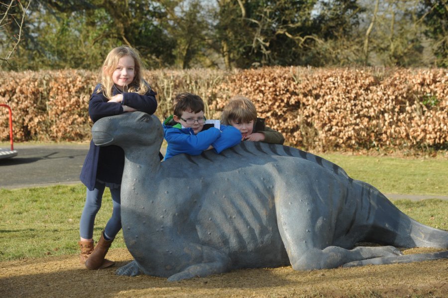 Three children leaning on the Cuckfield Iguanodon bronze sculpture