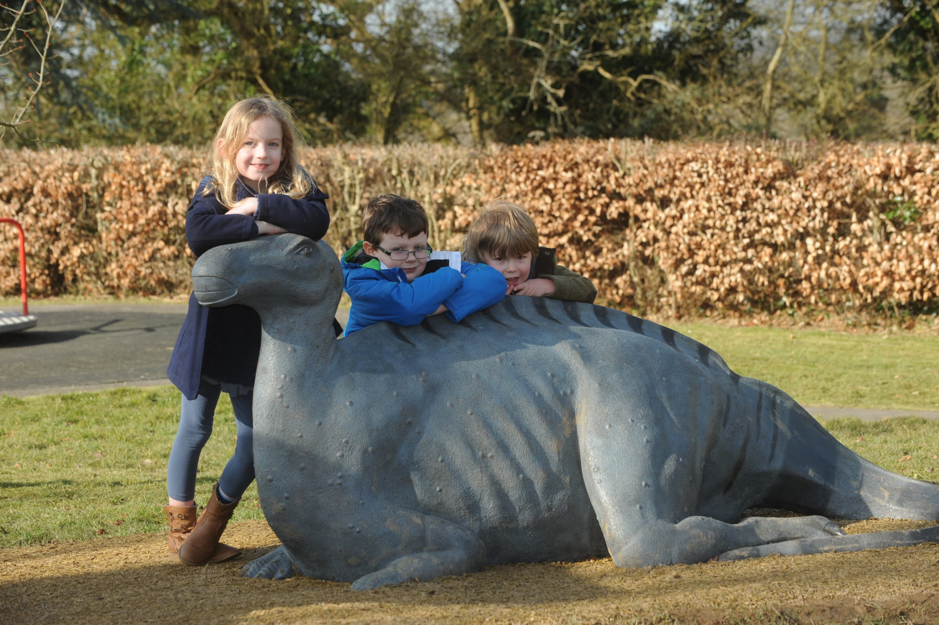 Three children leaning on Iguanodon bronze sculpture